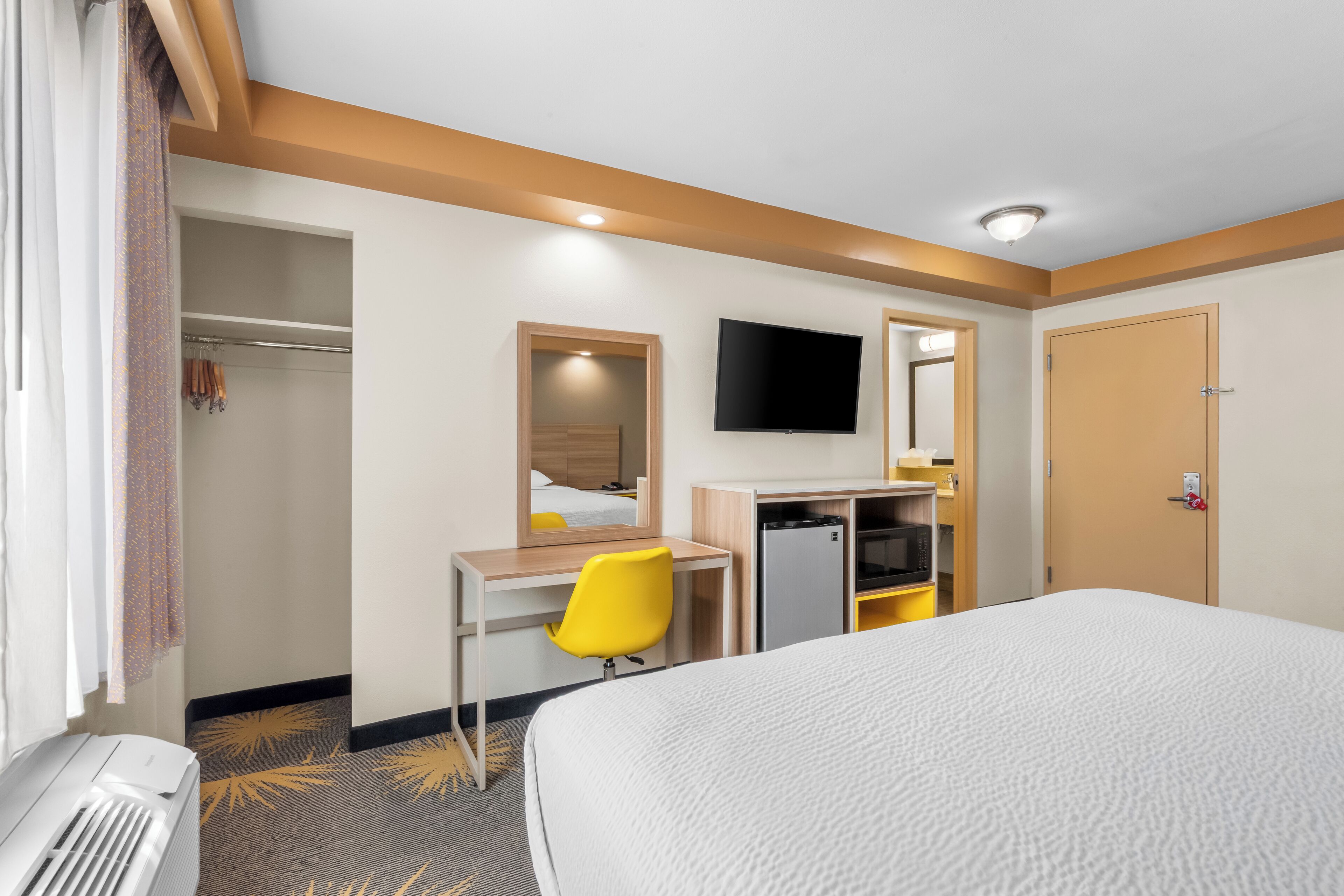 A hotel room with a bed, a desk with a chair, a television, a wardrobe, and a mirror.