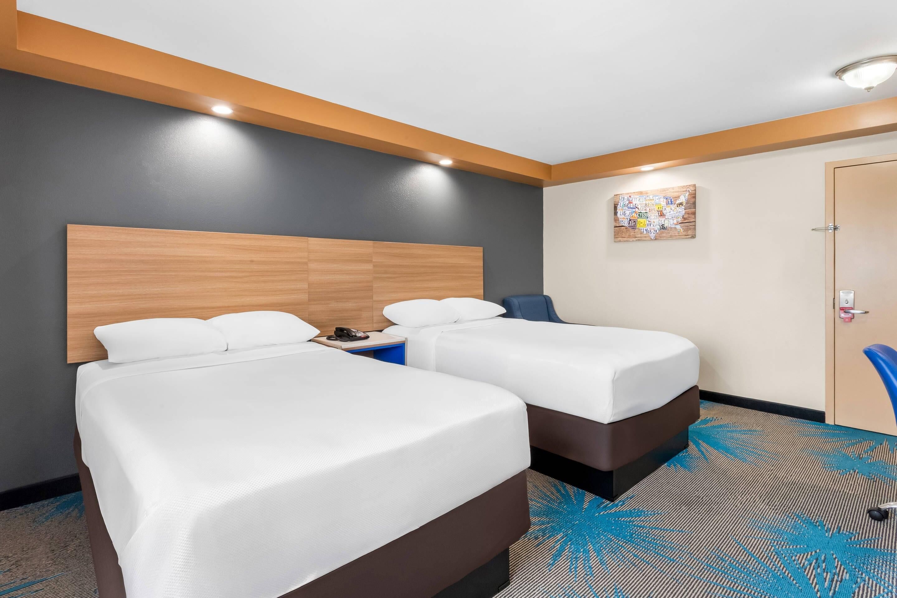 A hotel room with two beds, a wooden headboard, a small table, a chair, and a door.