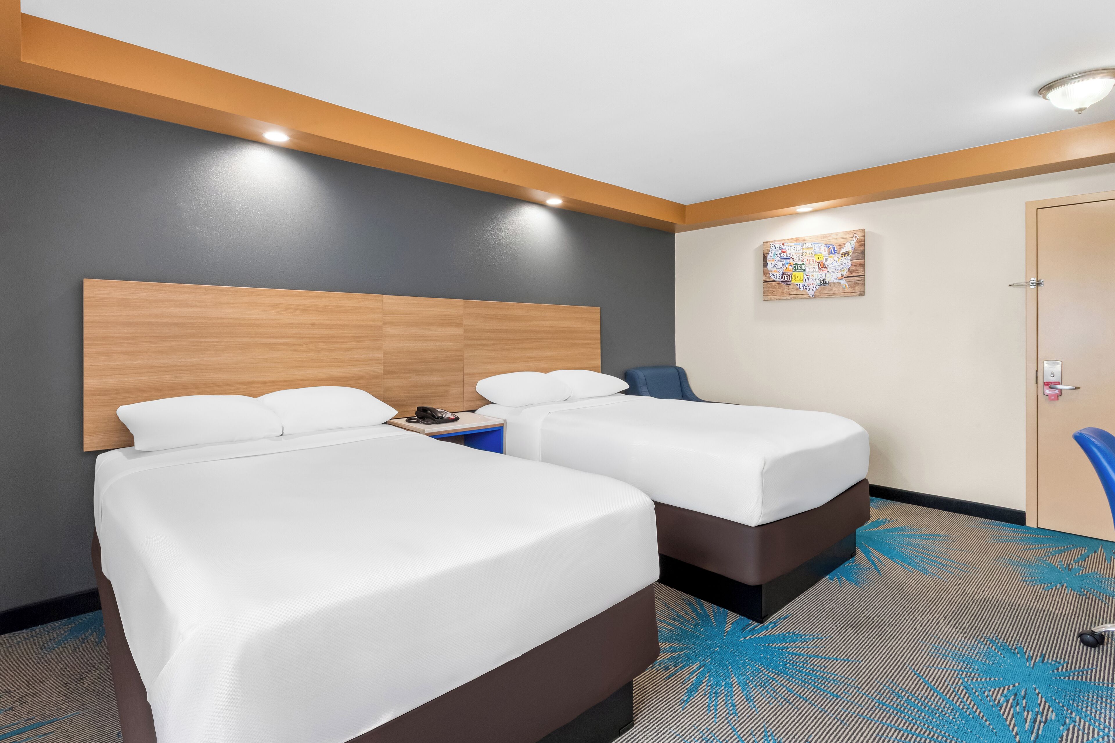 Habitación de hotel con dos camas, cabecero de madera, una silla azul y alfombra estampada en azul.