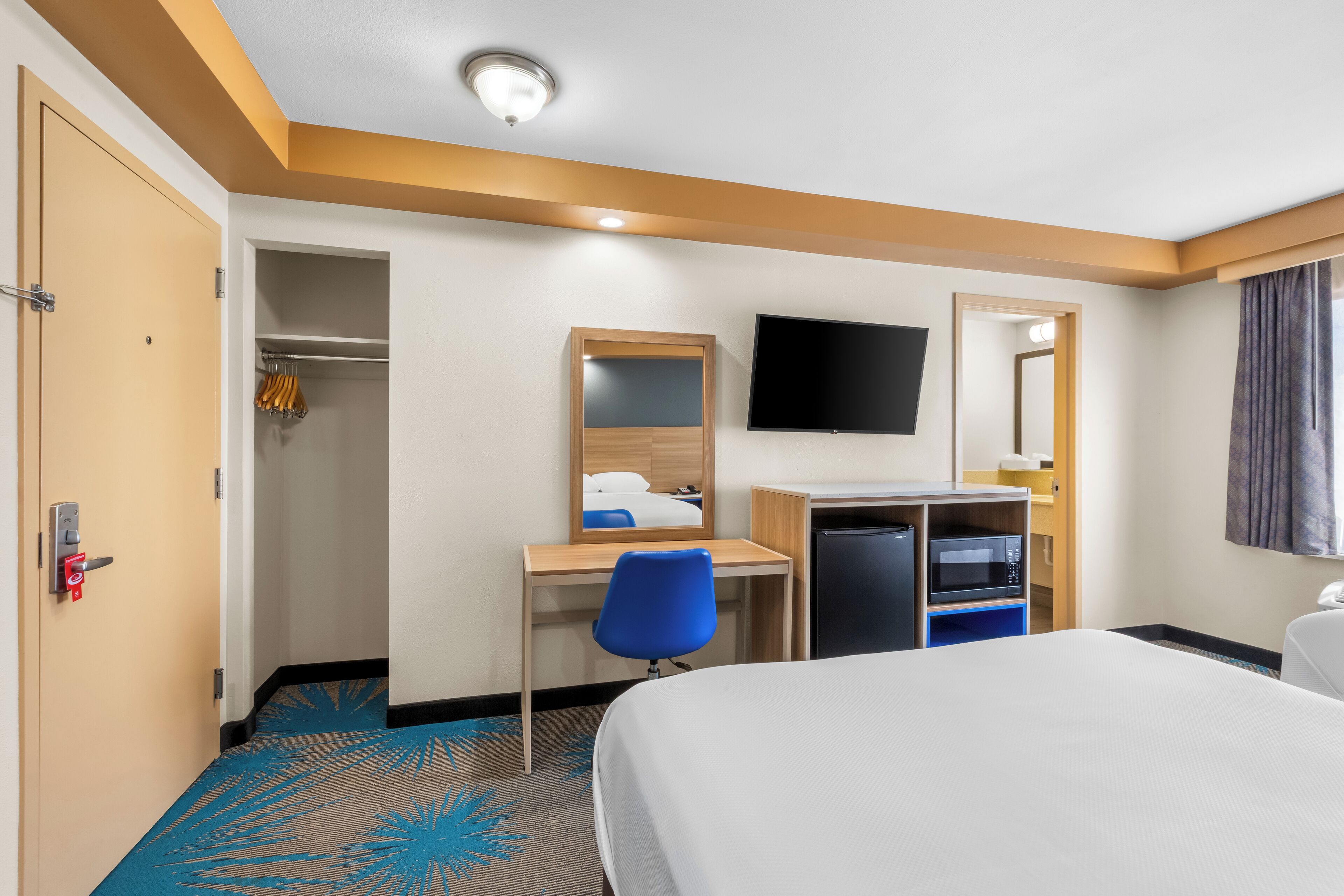 Een hotelkamer met een bed, een bureau met stoel, een televisie, een spiegel en een kledingkast.