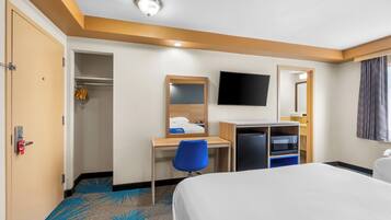 Een hotelkamer met een bed, een bureau met stoel, een televisie, een spiegel en een kledingkast.