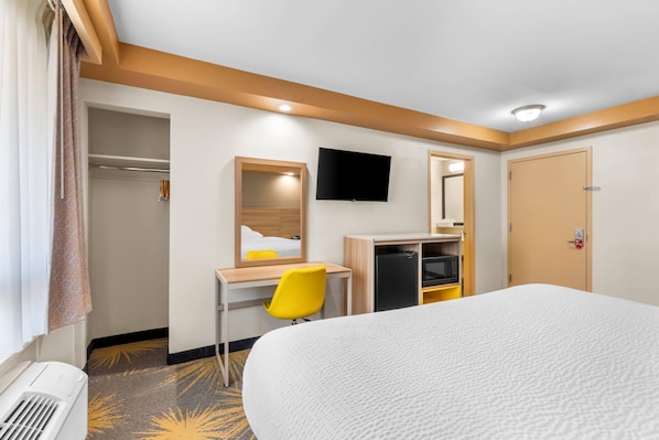 A hotel room with a bed, a desk with a chair, a television, and a wardrobe.