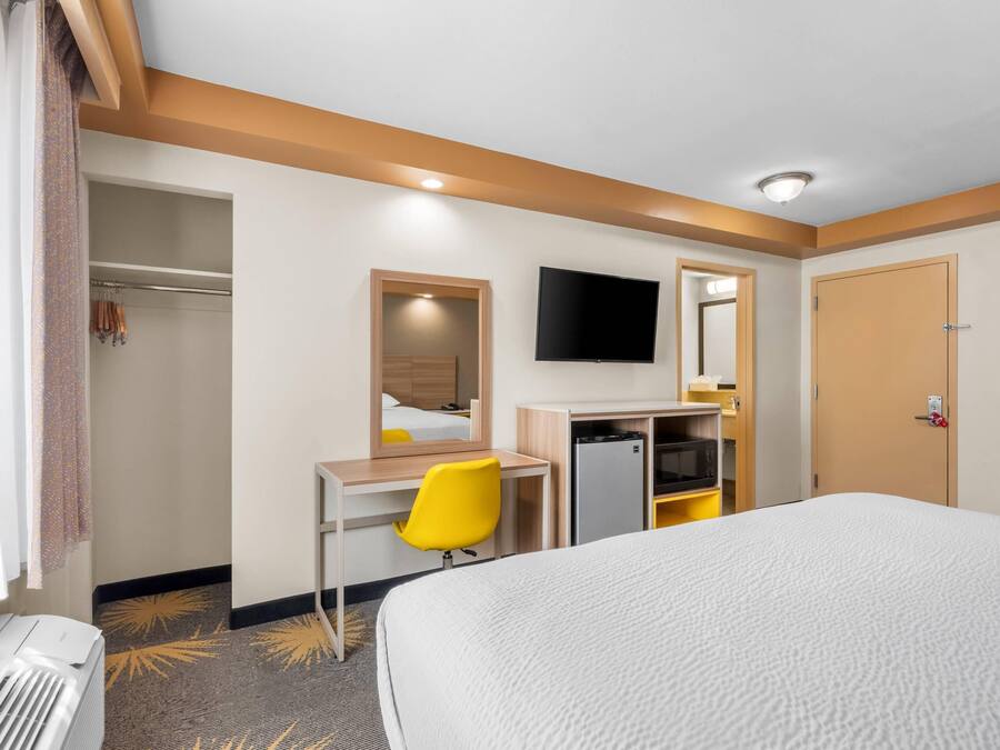 A hotel room with a bed, a desk with a chair, a TV, and a wardrobe.