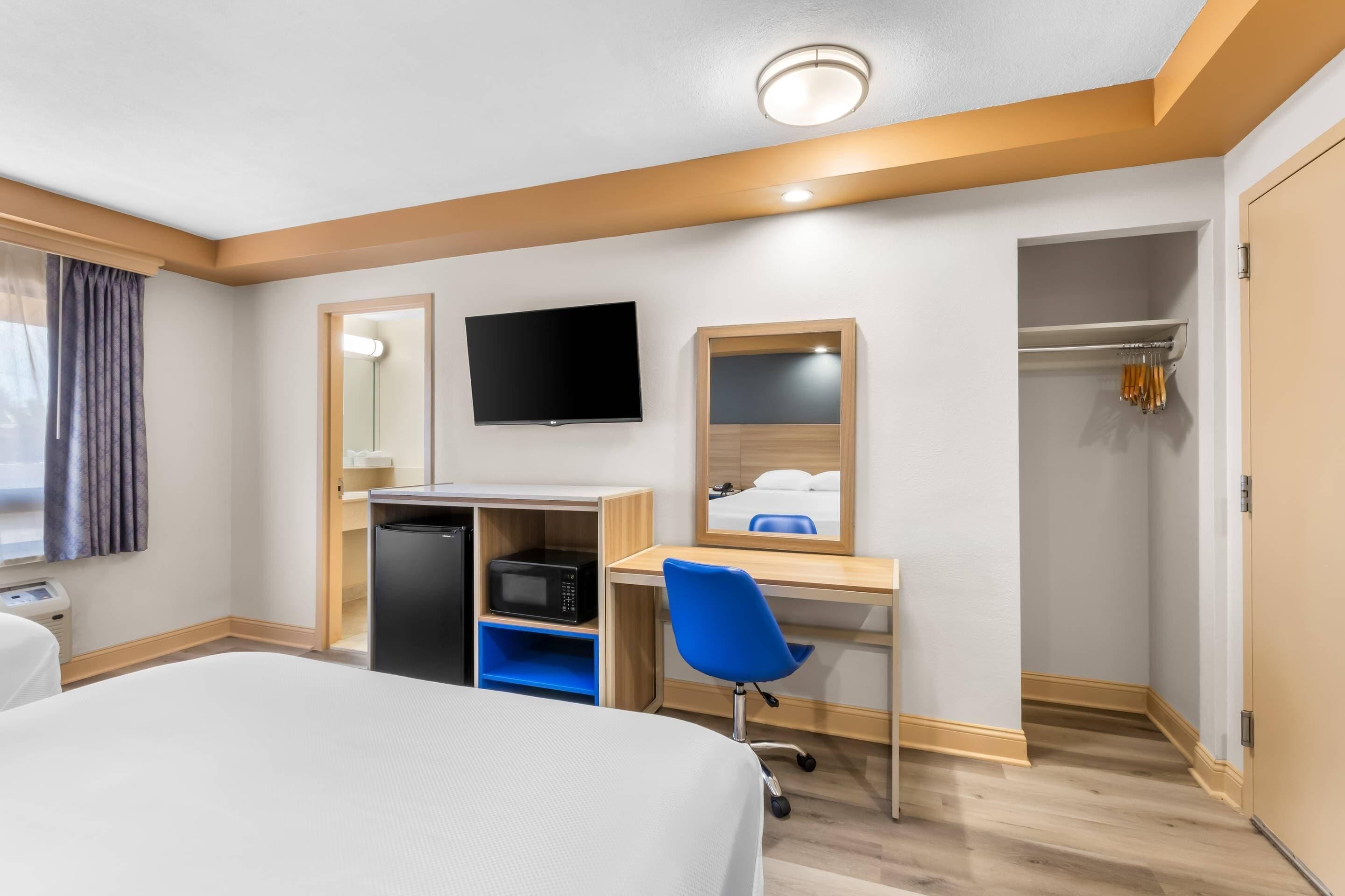 Une chambre d’hôtel comprenant un lit, un bureau avec un ordinateur, une télévision, un miroir, une armoire et une douche.