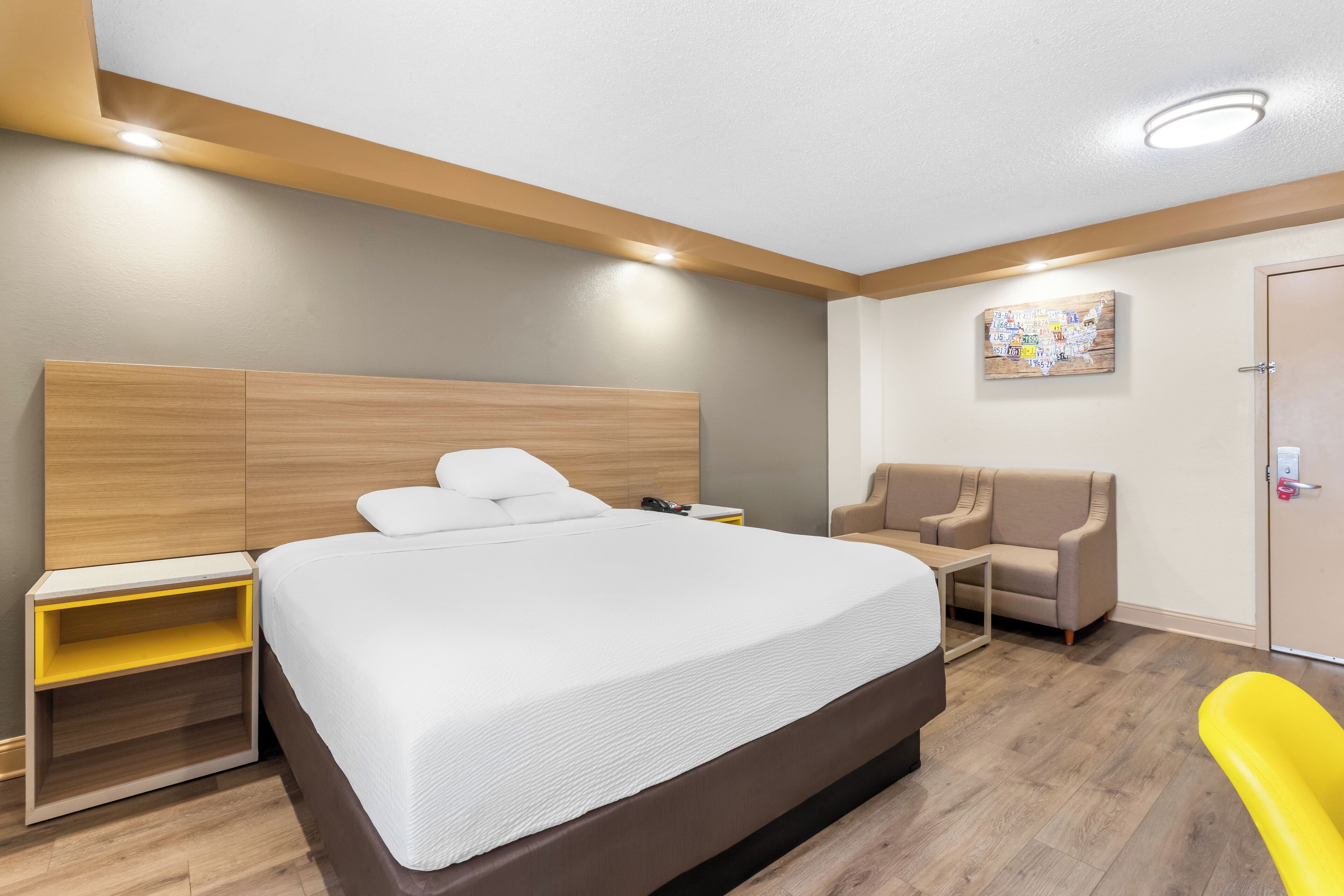 Een moderne hotelkamer met een groot bed, een houten hoofdbord, een bureau met stoel, een bank en een kleine tafel.