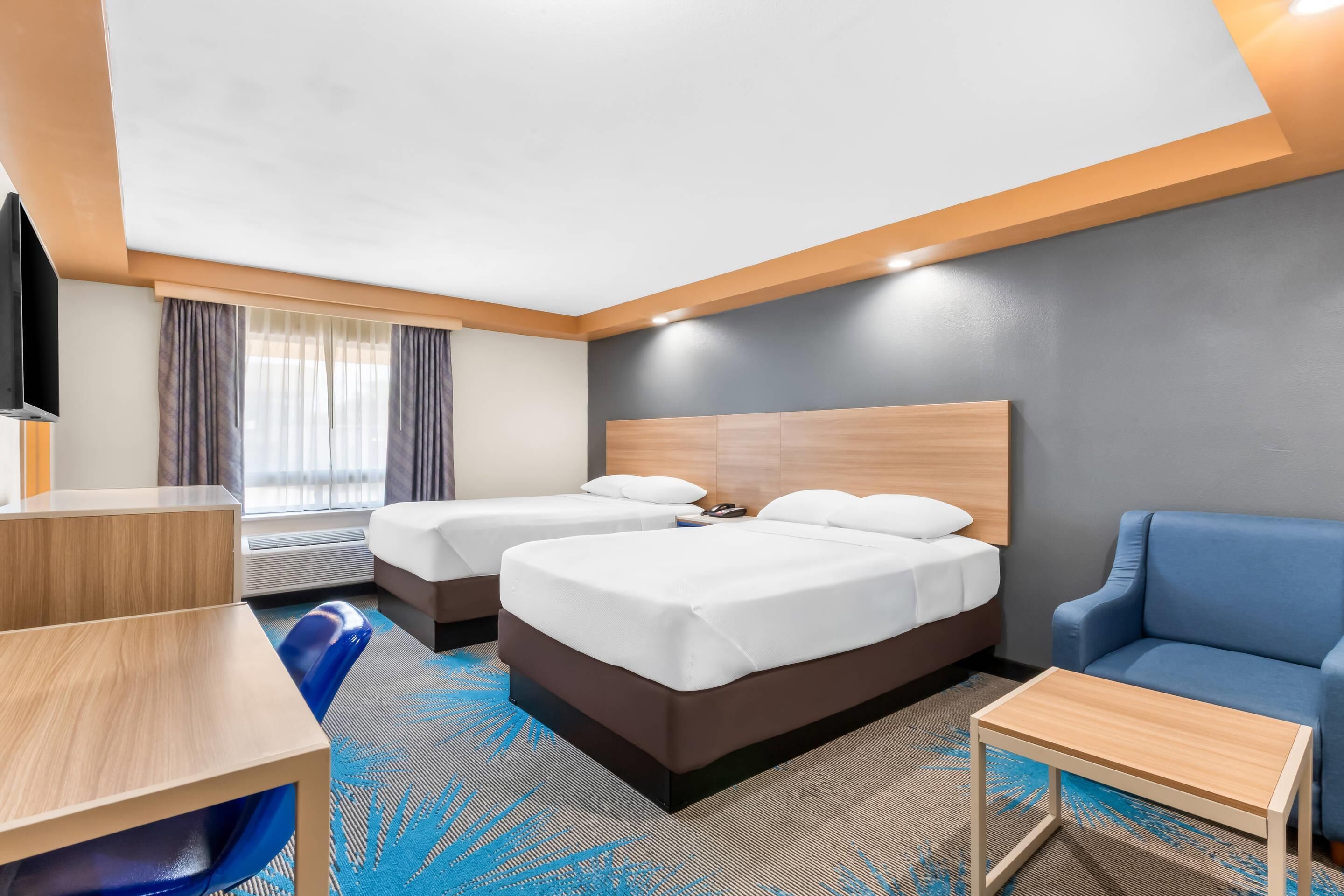 A hotel room with two beds, a desk, a chair, and a TV.