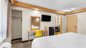A hotel room with a bed, a desk with a chair, a television, a wardrobe, and a mirror.