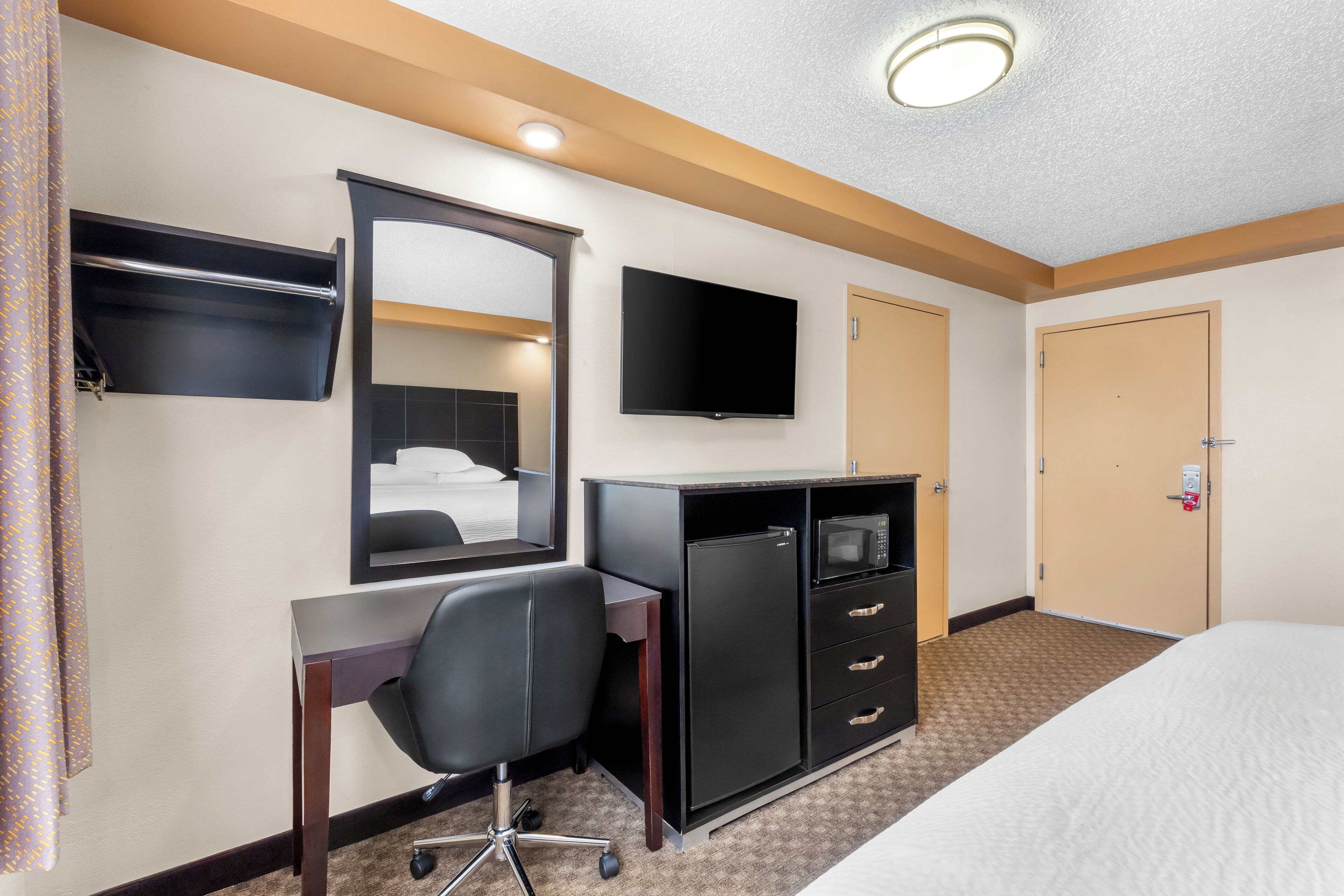 Habitación de hotel con cama, escritorio, silla, televisión, minibar y armario.