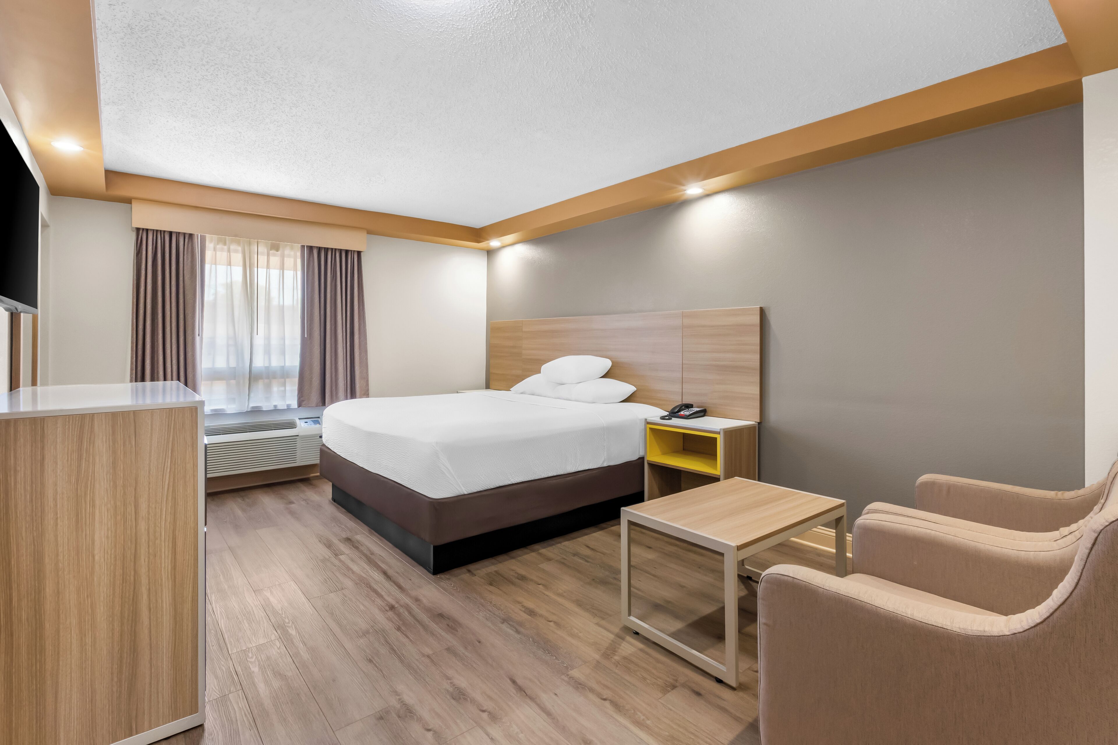 A modern hotel room with a bed, bedside table, chair, and a small desk.