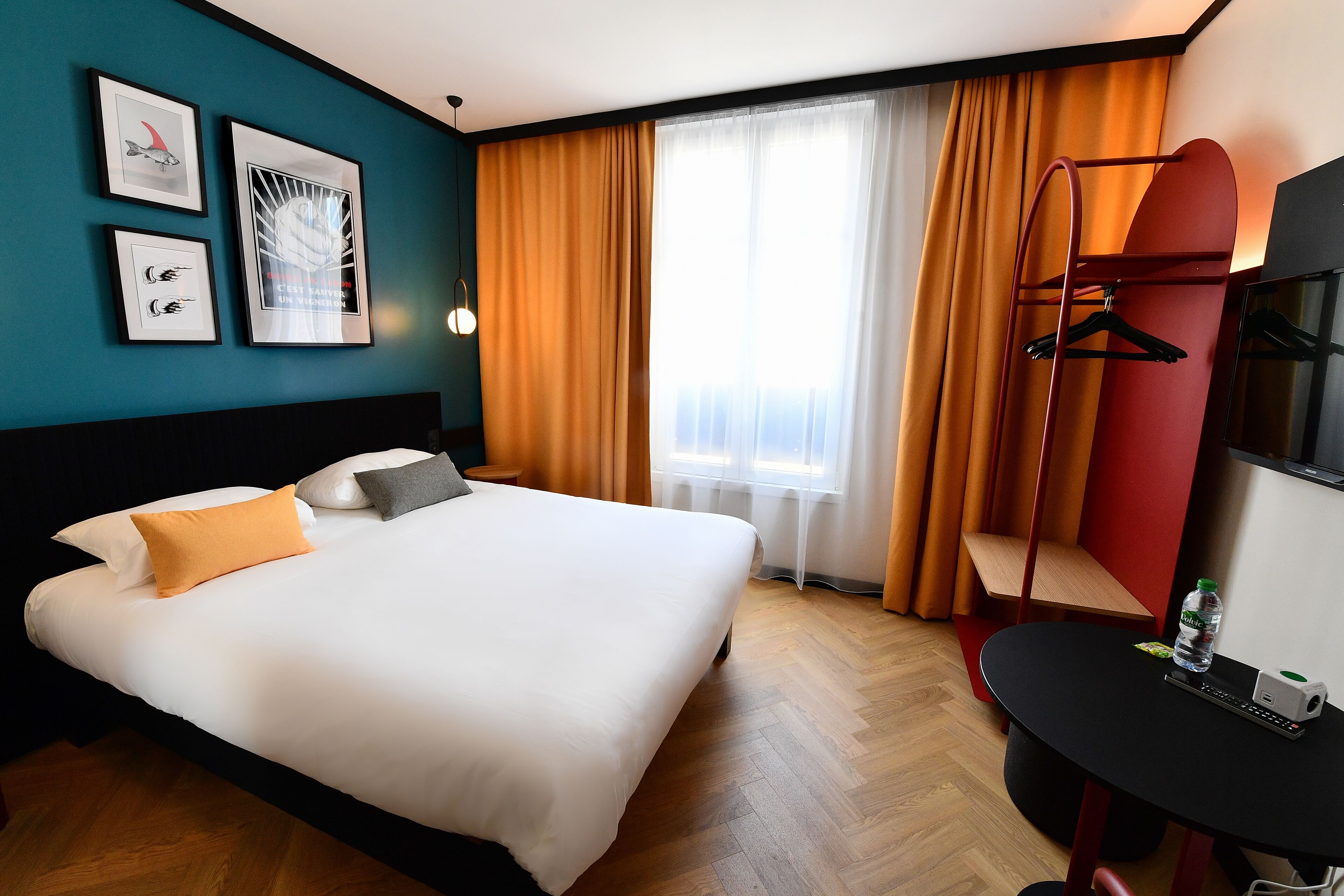 Een hotelkamer met een bed, een bureau, een stoel, een televisie en een raam met gordijnen.