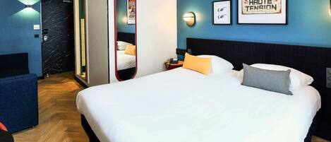 A hotel room with a large bed, a bedside table with a lamp, a mirror, and framed pictures on the wall.