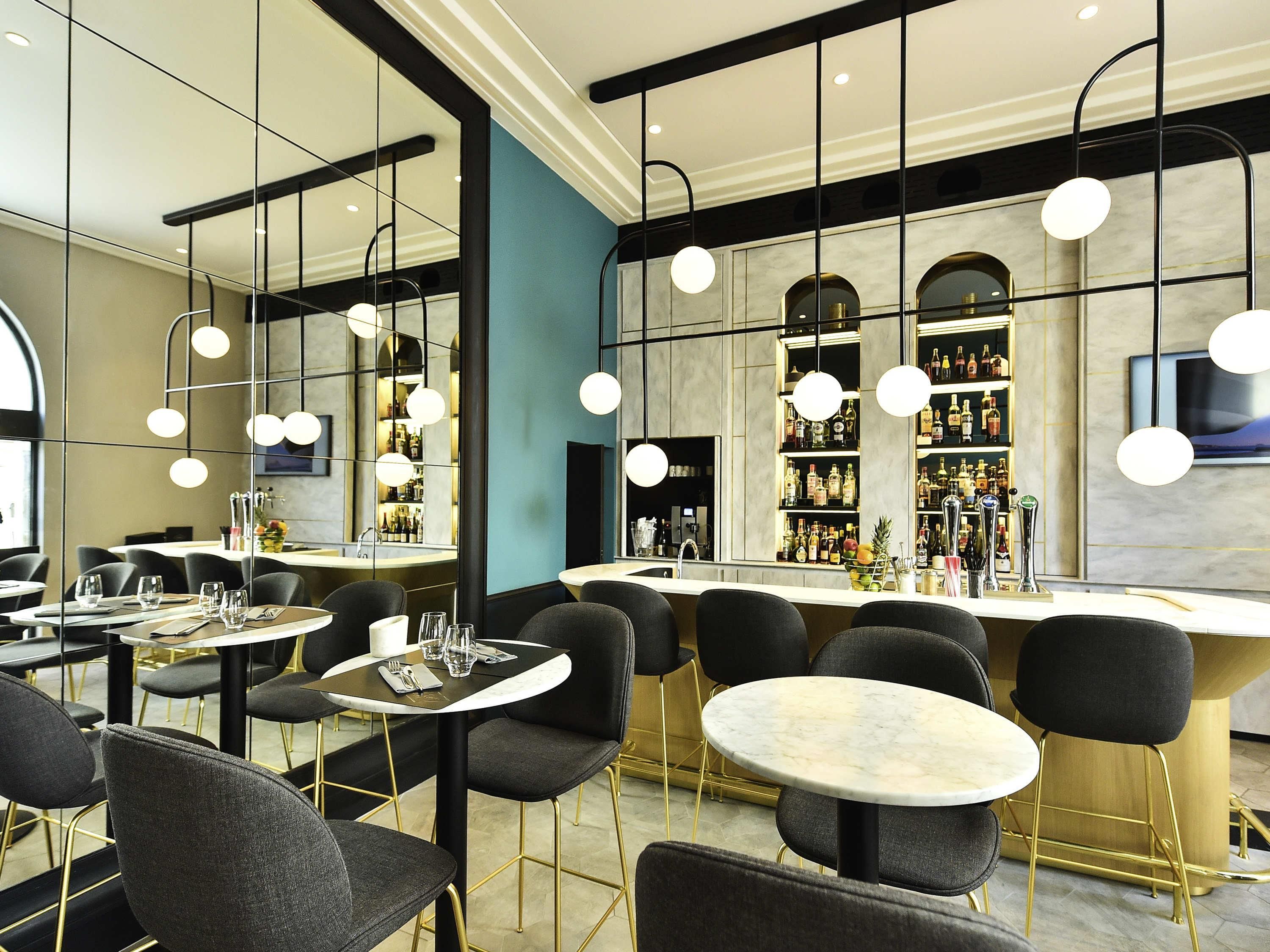 Un espacio moderno de bar con mesas redondas, sillas negras y una estantería repleta de licores.