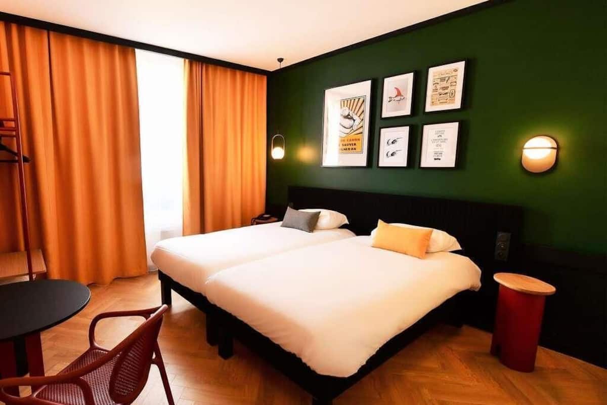 Una habitación de hotel con dos camas, un escritorio, una silla y una pared decorada con cuadros.
