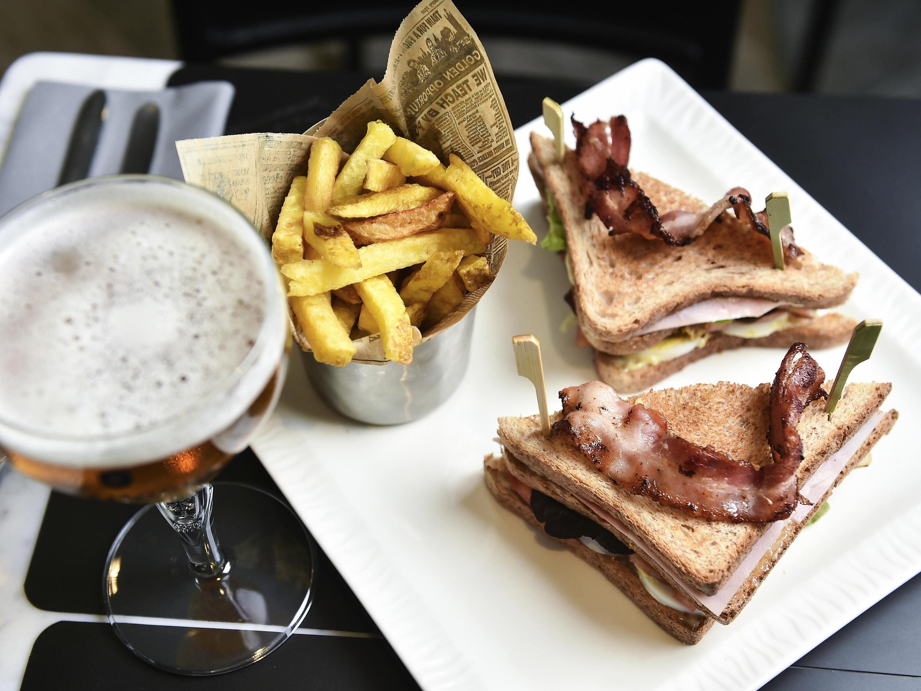 Un repas composé d’un sandwich au bacon, d’un verre de bière et d’une petite portion de frites.