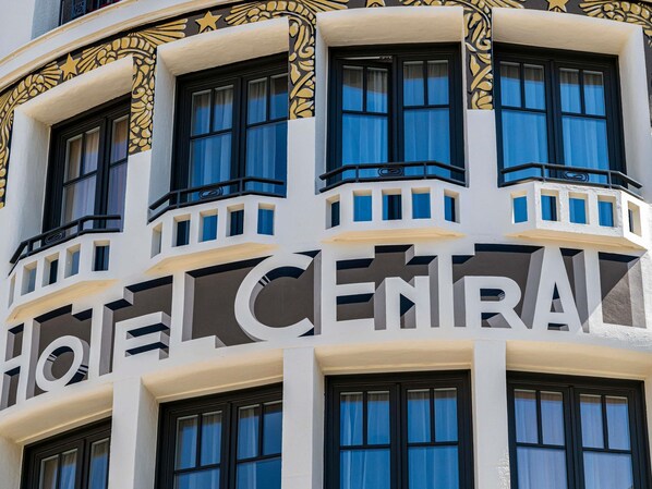 A building with a large sign reading 'HOTEL CENTRAL' and multiple windows with black frames and blue curtains.