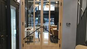 Puerta de madera con paneles de vidrio, escalera con barandilla y un cartel que indica un baño.