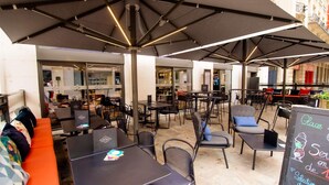 Un café al aire libre con mesas, sillas, sombrillas y un menú en una pizarra.