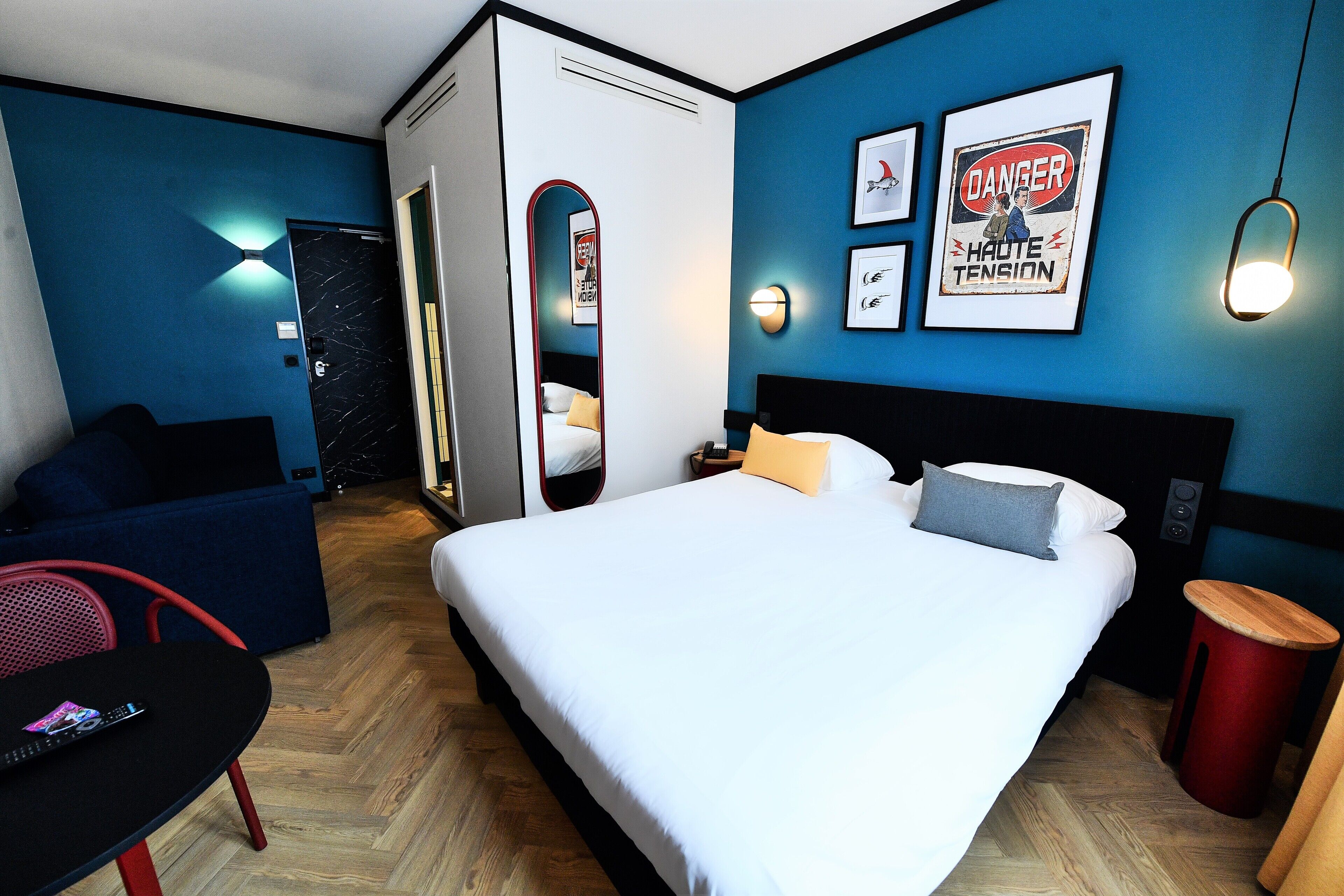 A hotel room with a bed, a desk, a chair, and a red trash bin.