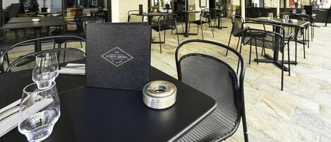Un café al aire libre con mesas y sillas, un atril con la carta y vistas a la calle.