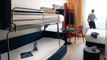 A hotel room with bunk beds, a desk, a chair, a small table, and a window with curtains.