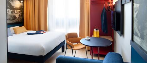 A hotel room with a bed, a blue sofa, a small table, and a TV mounted on the wall.