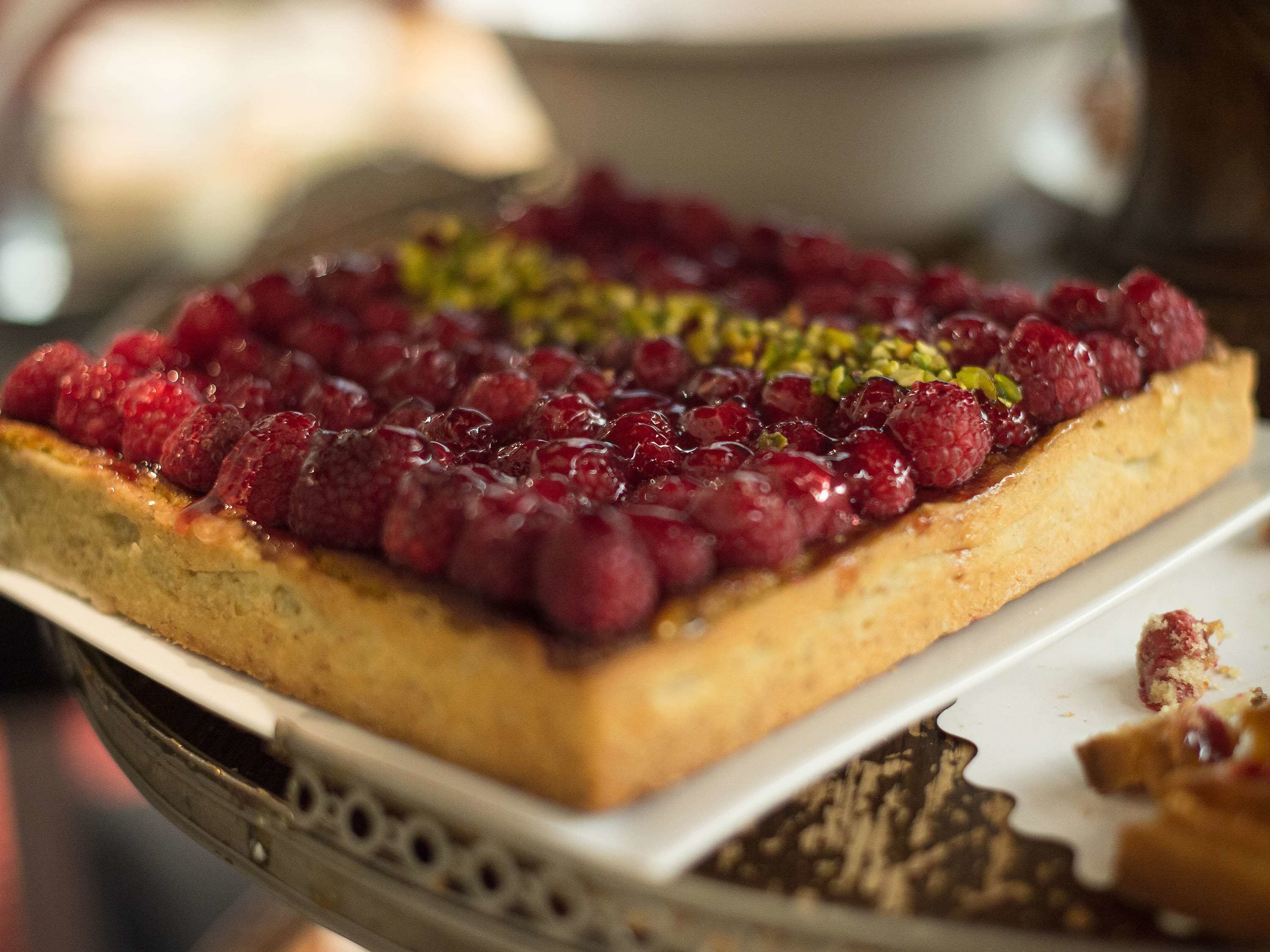 A square tart topped with raspberries and pistachios.