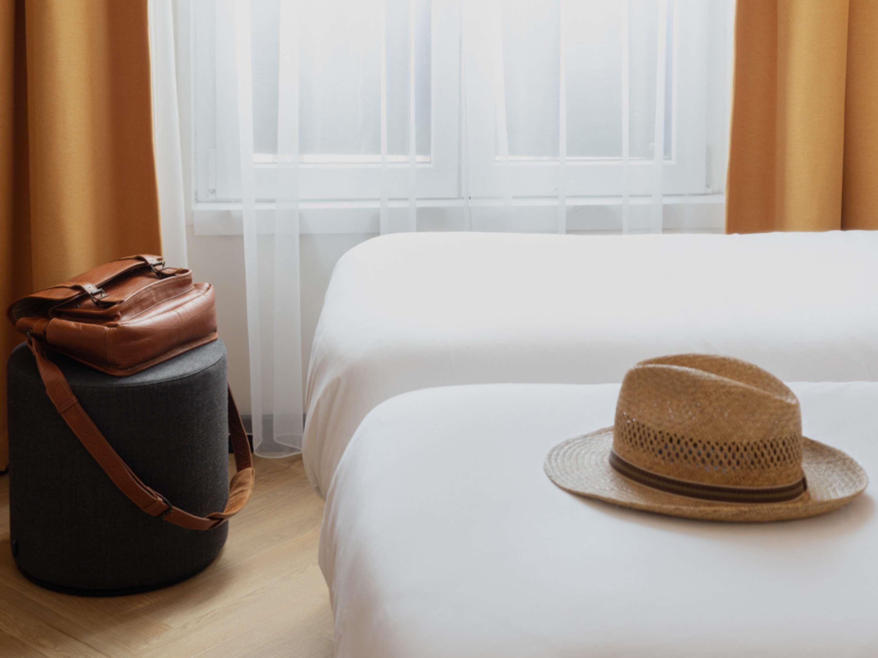 Une chambre d’hôtel avec un lit, une valise et un chapeau posé sur le lit.