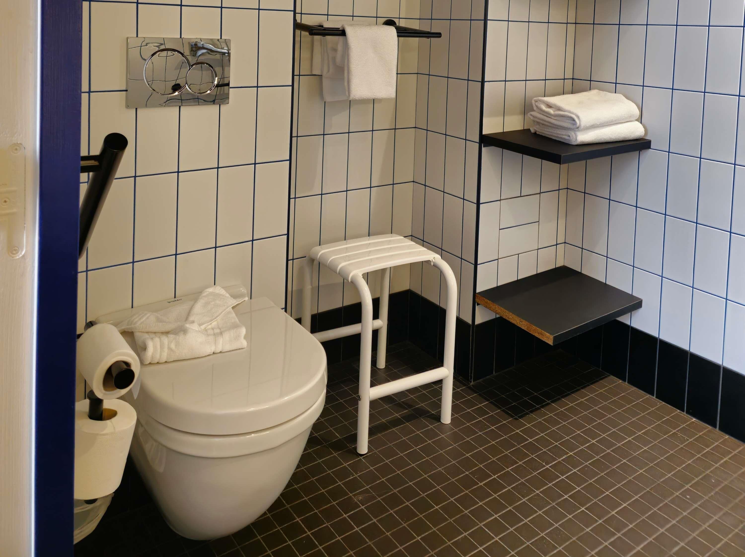 Ein kleines, modernes Badezimmer mit Toilette, einem weißen Waschbecken, einem Handtuchhalter und einem Regal mit gefalteten Handtüchern.