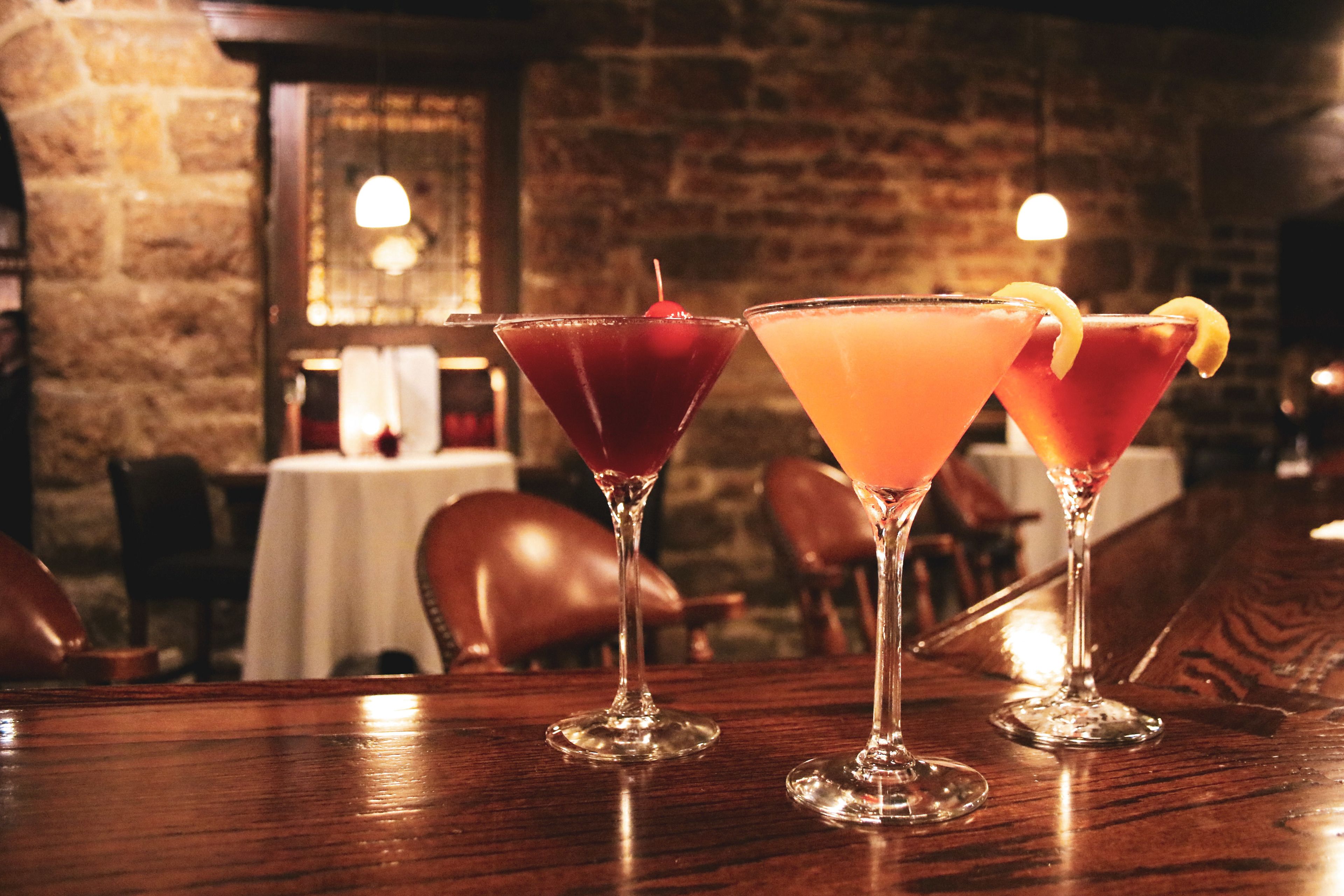 Tres copes de martini sobre una taula de fusta en un restaurant amb parets de pedra i sostre de rajola.