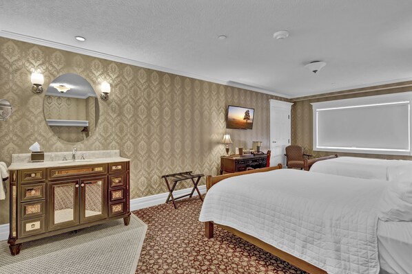 A hotel room with a large bed, a vanity with a mirror, a television, and a desk with a lamp.