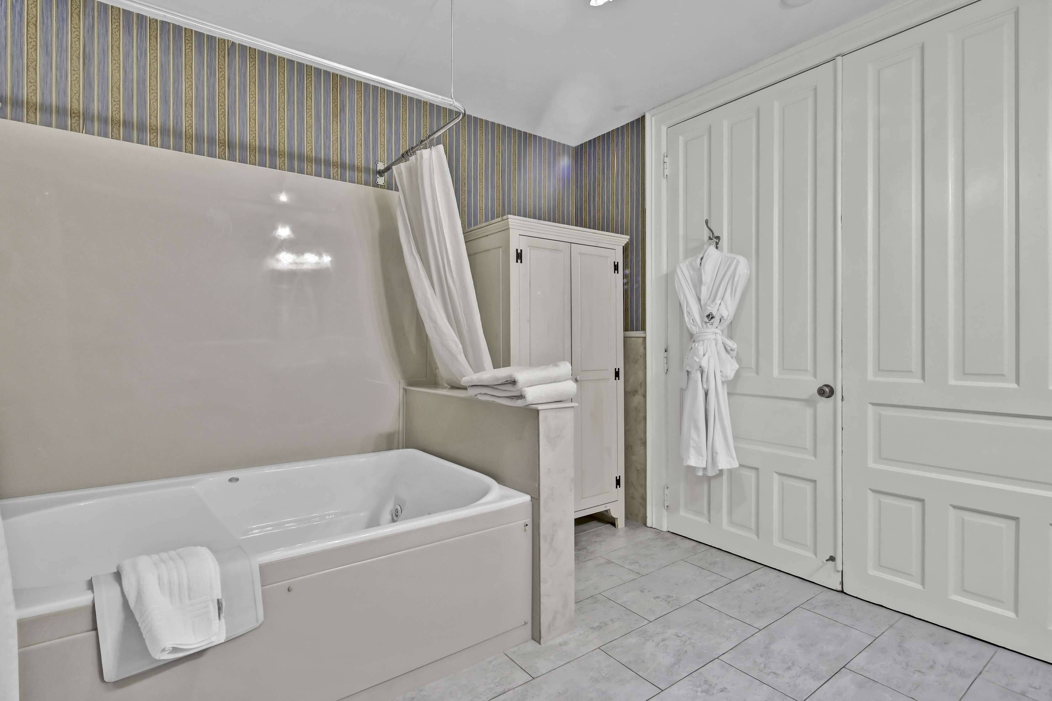 A modern bathroom with a bathtub, a shower curtain, a robe hanging on the door, and a cabinet.