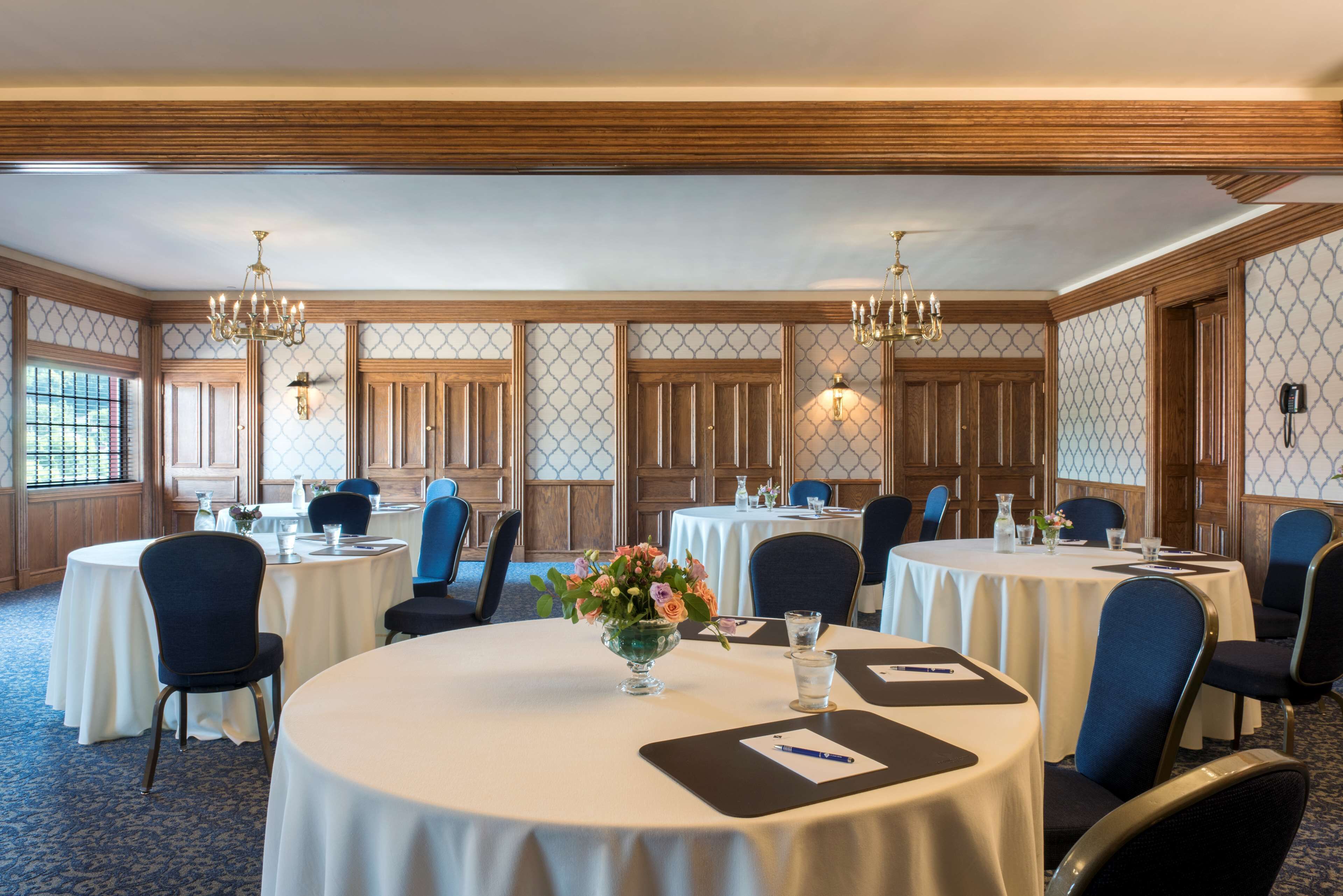 A conference room with round tables, blue chairs, and chandeliers.