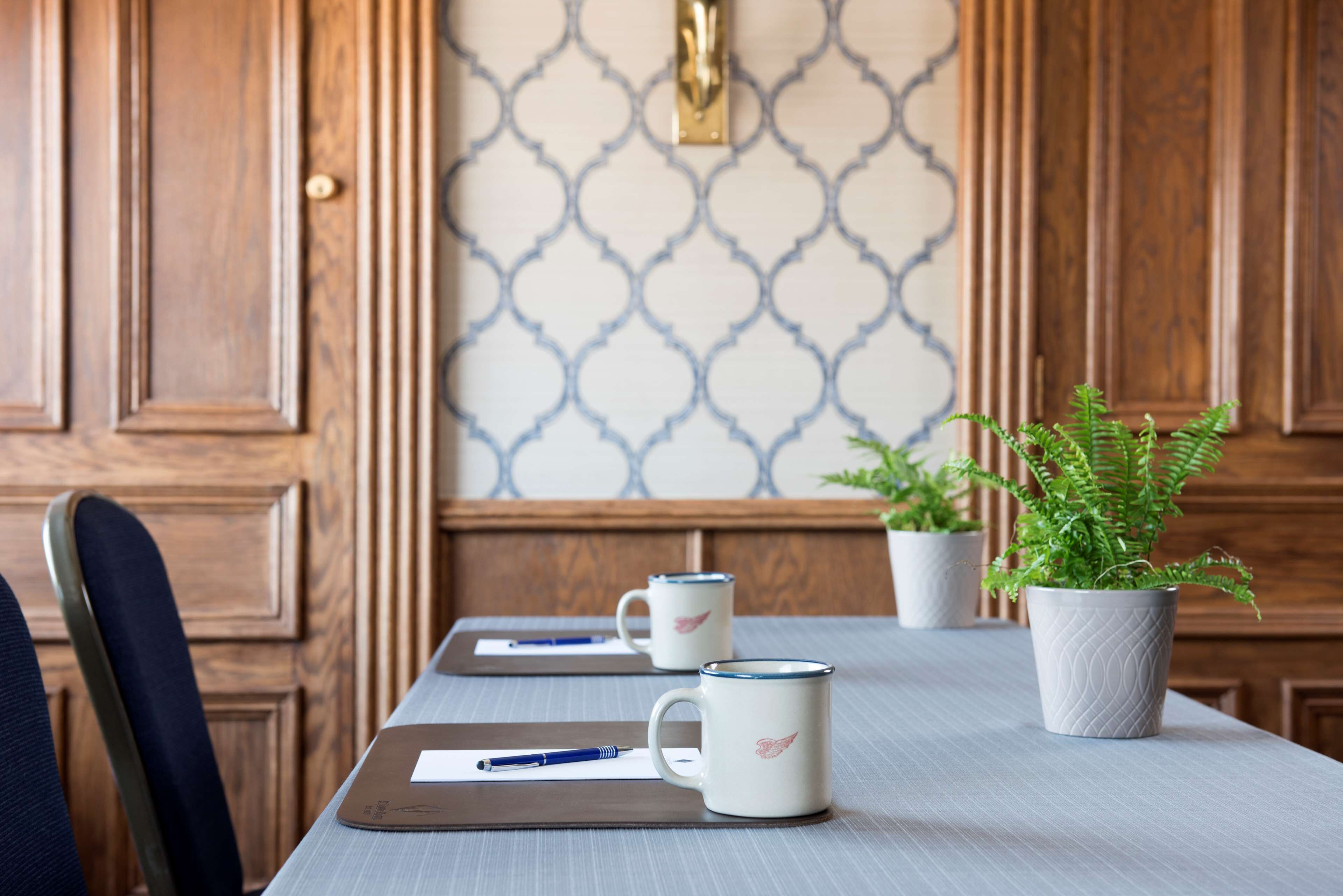 Una mesa de madera con dos tazas blancas, un cuaderno y un bolígrafo. Hay una planta en maceta sobre la mesa.