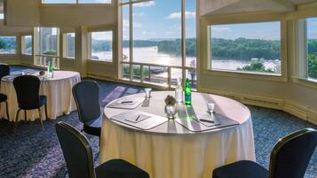 Un salón de conferencias con mesas redondas, sillas y grandes ventanales con vistas al río.