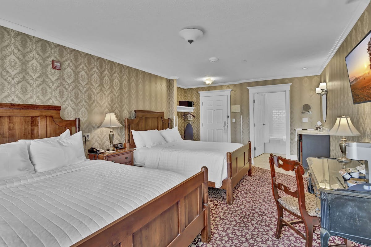 Een hotelkamer met twee bedden, een houten hoofdeinde, een bureau met een lamp en een stoel.