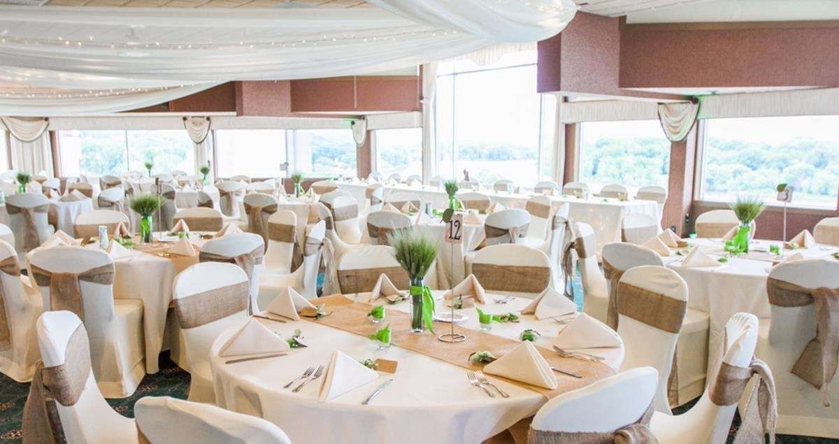 Uma sala de banquetes com mesas redondas, cadeiras brancas e centros de mesa verdes.