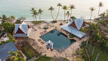 A resort with a swimming pool, lounge chairs, and palm trees.