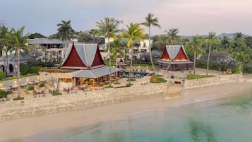 A beachfront resort with multiple buildings, a pool, and palm trees.