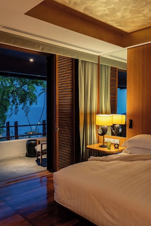 A hotel room with a bed, a nightstand with a lamp, a view of the ocean, and a balcony with a railing. - Chiva-Som Hua Hin (Hua Hin)