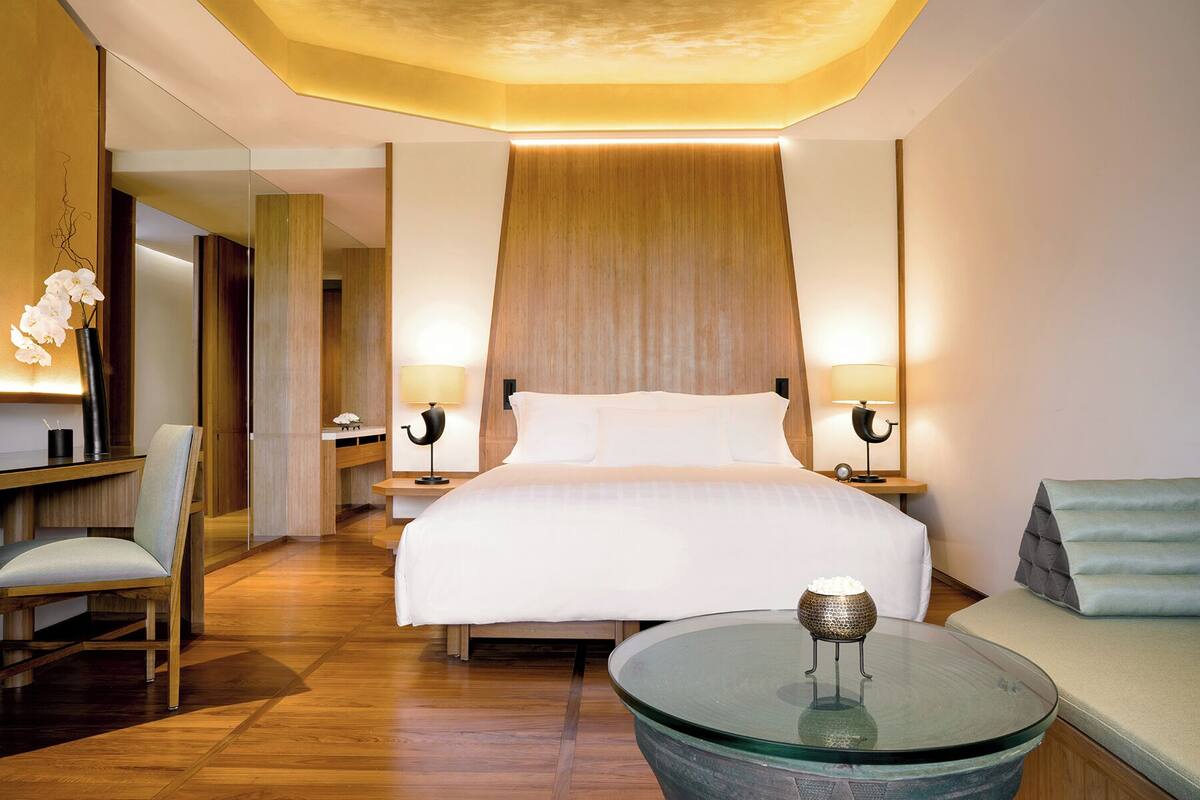 Een hotelkamer met een groot bed, twee nachtkastjes met lampen, een glazen salontafel, een bank en een houten vloer.