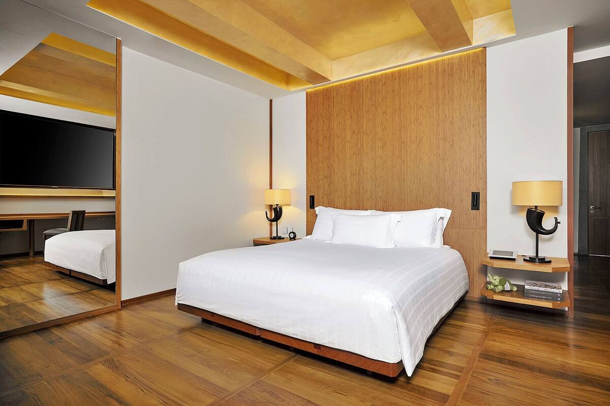 Een moderne hotelkamer met een groot bed, houten vloeren en een grote spiegel aan de muur.