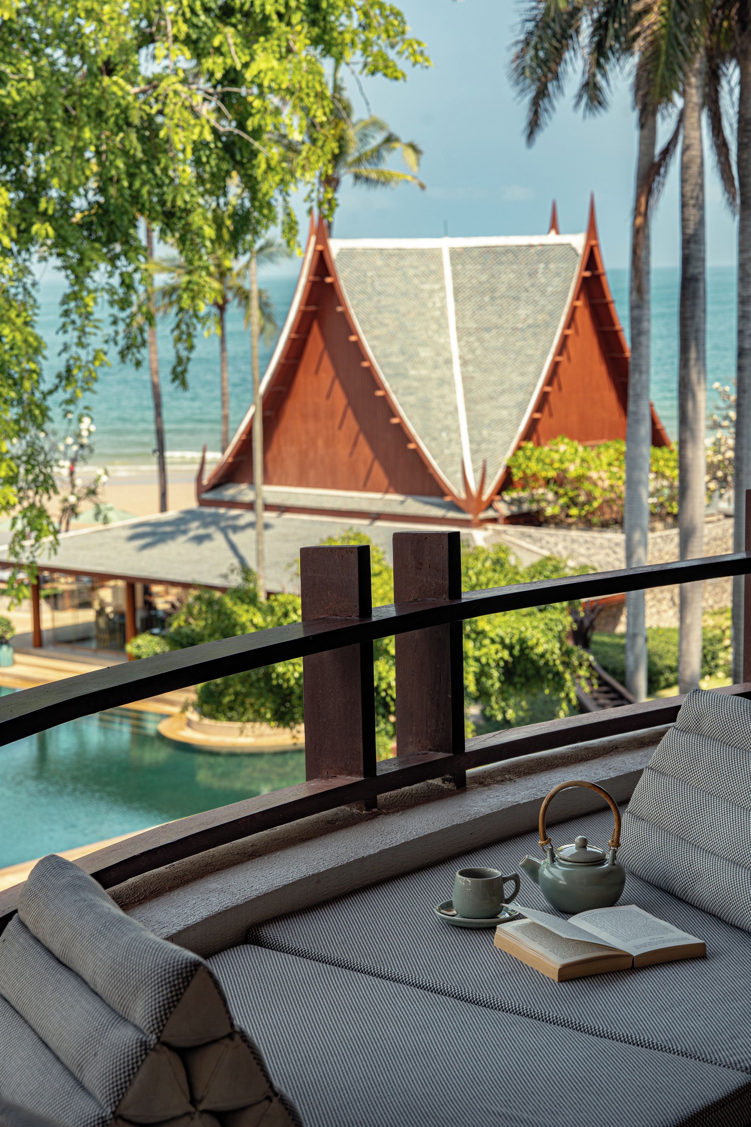 A balcony with a view of a traditional building by the sea, a teapot, and a book.