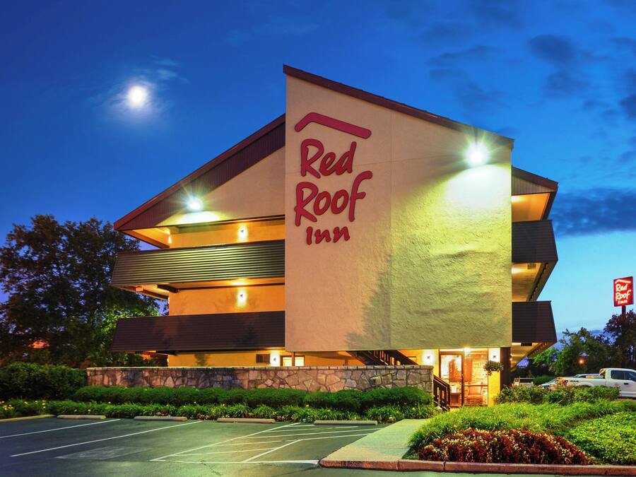 A Red Roof Inn building with a modern design, a stone facade, and a parking lot in front.