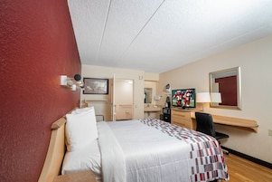 Habitación de hotel con cama, escritorio, televisión y espejo.