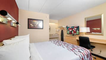 Habitación de hotel con cama, escritorio, televisor y espejo.