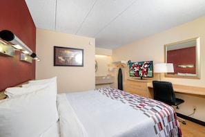 Habitación de hotel con cama, escritorio, televisor y espejo.