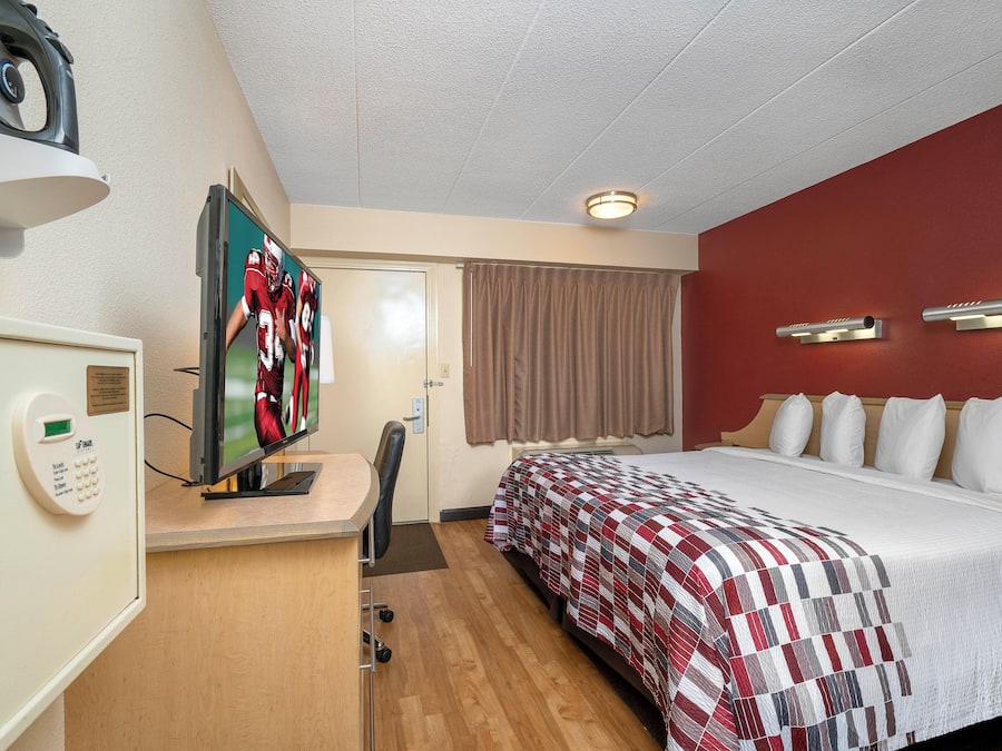 A hotel room with a bed, a desk with a television, a door, and a window with curtains.