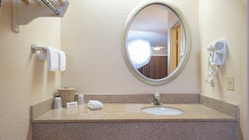 A bathroom with a granite countertop, a sink, a mirror, a towel rack, a trash can, and a hairdryer.