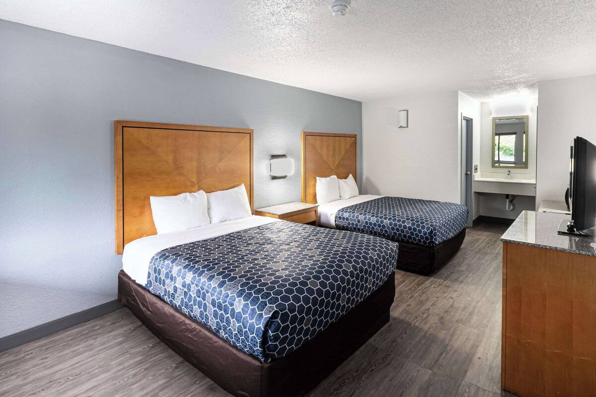 A hotel room with two beds, a desk, a TV, and a bathroom visible through an open door.