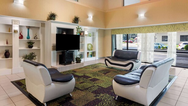 A spacious living room with two white leather sofas, a flat-screen TV, and a variety of decorative items on shelves. - Rodeway Inn At Fort Lee (Hopewell)
